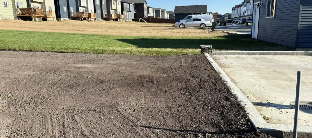 Compact skid steer equipment performing residential final grading and topsoil leveling services on a new home build in Edmonton.
