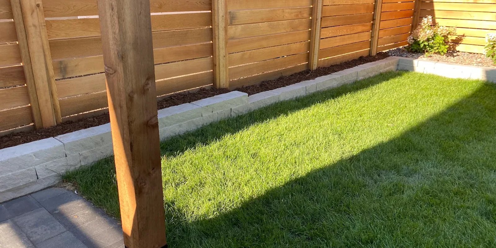 A newly installed structural retaining wall and pressure-treated wood fence built in an Edmonton residential backyard to manage a steep slope and provide privacy.