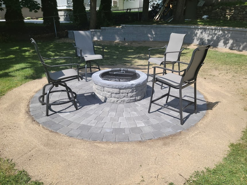Beautiful stone patio with modern outdoor seating and lush landscaping, perfect for relaxing in a stylish backyard setting.
